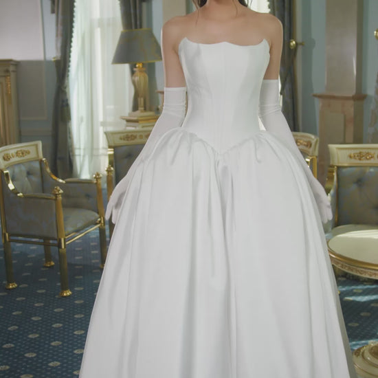 Mikado A-line wedding dress with reverse sweetheart neckline, drop-down waspie corset, sleeveless design, long gloves, zip closure, and flowing chapel train for elegant modern bridal look