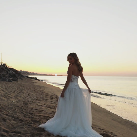 Bride in strapless lace corset wedding dress with fringe detail, lace-up back, soft tulle A-line skirt with slit, and court train.