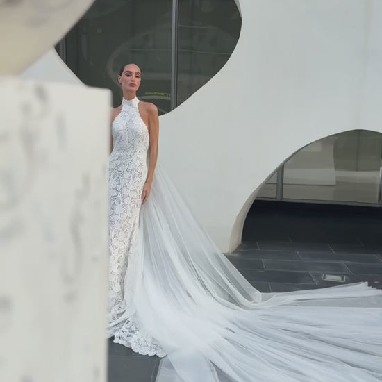 Backless halter lace sheath wedding dress with detachable tulle overskirt and cathedral train, photographed in the city.
