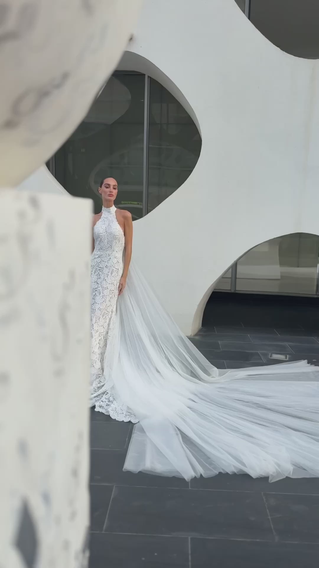 Backless halter lace sheath wedding dress with detachable tulle overskirt and cathedral train, photographed in the city.