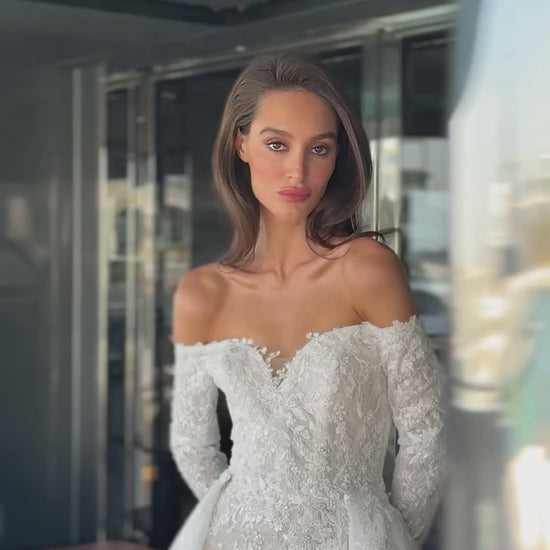 Camber off-shoulder lace wedding gown with detachable tulle overskirt. A romantic mermaid silhouette with illusion sleeves, hand-applied lace, and a sculpted corset bodice for two stunning bridal looks in one.