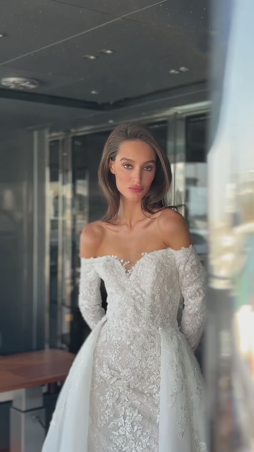 Camber off-shoulder lace wedding gown with detachable tulle overskirt. A romantic mermaid silhouette with illusion sleeves, hand-applied lace, and a sculpted corset bodice for two stunning bridal looks in one.