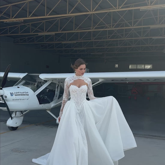 Bride wearing lace long-sleeve wedding dress with high illusion neckline, fitted corset bodice, and chapel train, featuring intricate lace cuffs and back detailing.