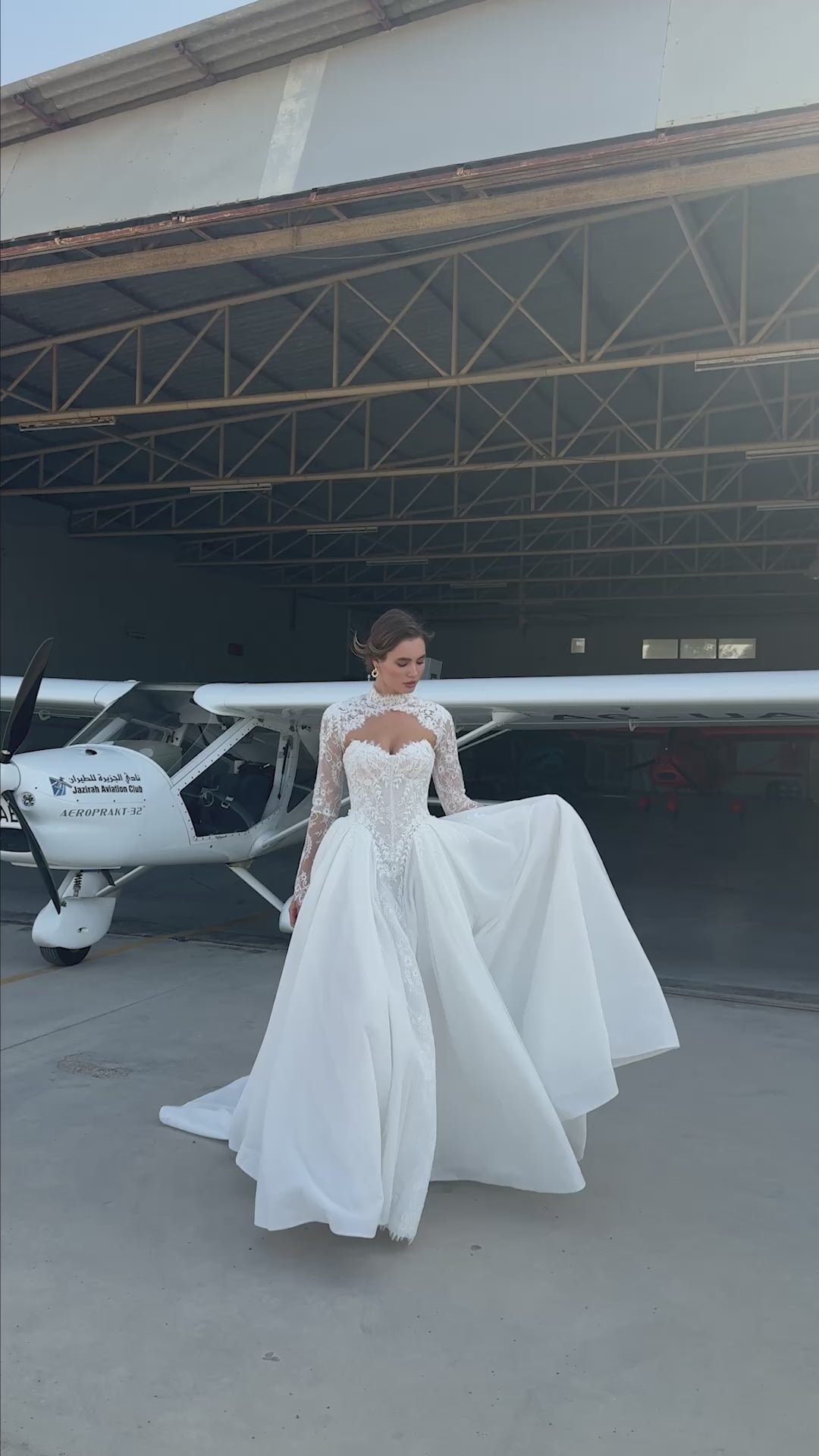 Bride wearing lace long-sleeve wedding dress with high illusion neckline, fitted corset bodice, and chapel train, featuring intricate lace cuffs and back detailing.