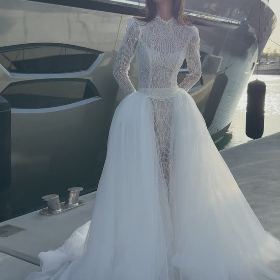 Celeste beaded lace long-sleeve sheath wedding dress with high neck and detachable tulle overskirt, open-back detail.