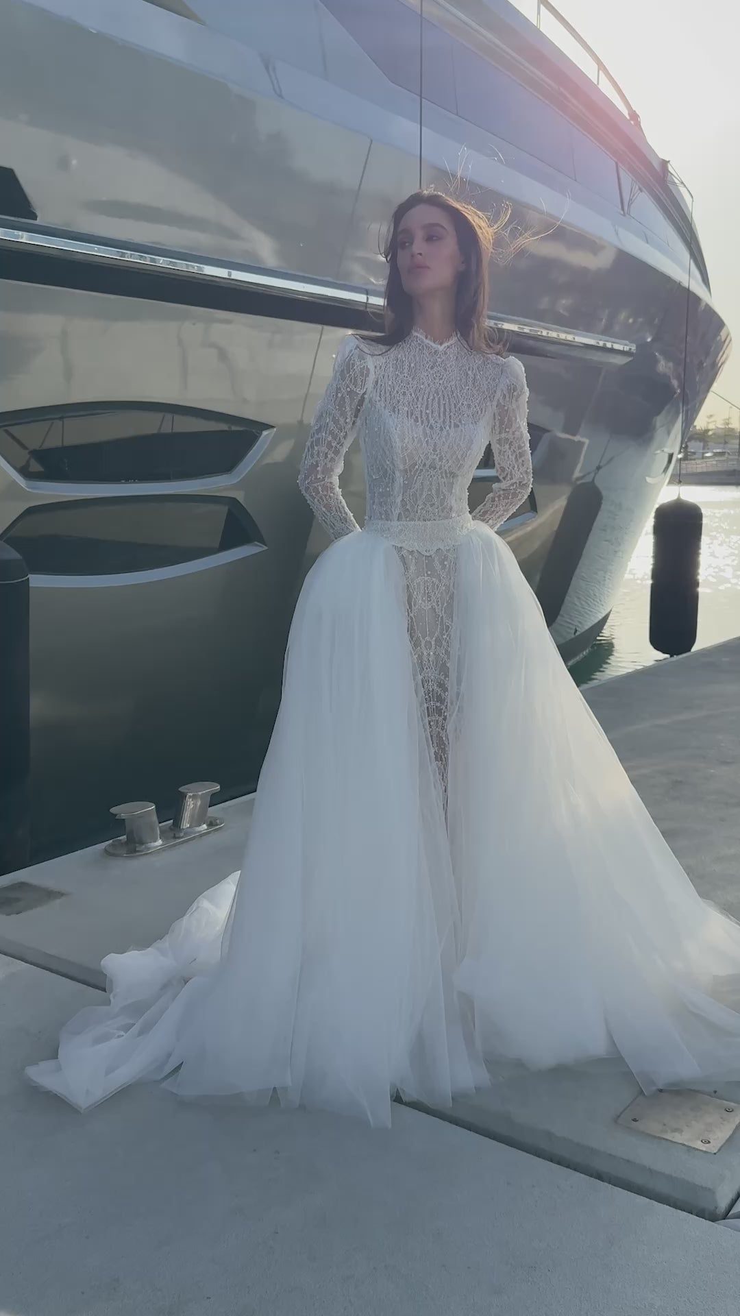 Celeste beaded lace long-sleeve sheath wedding dress with high neck and detachable tulle overskirt, open-back detail.