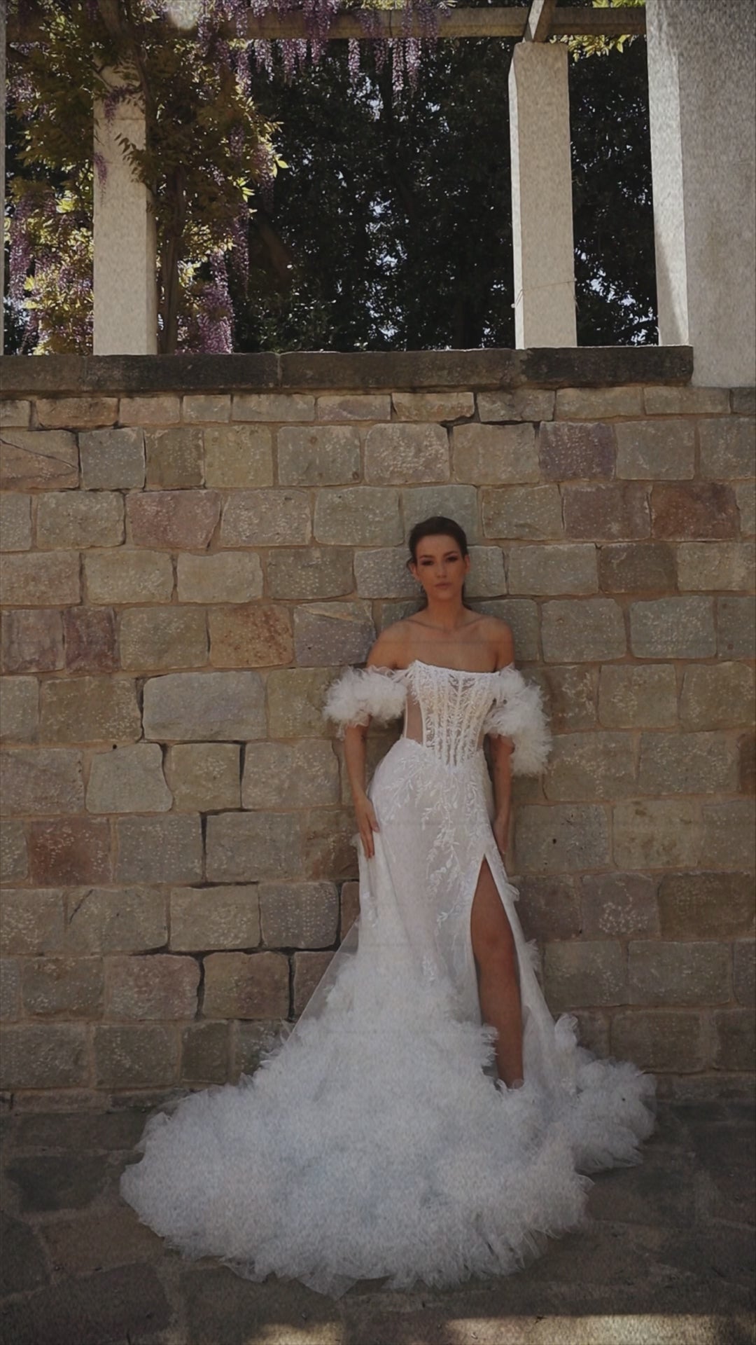 Bride in sleeveless tulle A-line wedding gown with pearl-adorned lace, 3D floral appliqués, boat neckline, slit skirt, drop waist, and straight open back.