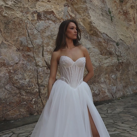 Princess A-line bridal gown with sleeveless sweetheart neckline, pearl-embellished sheer bodice, drop-down waist, slit skirt, and chapel train.