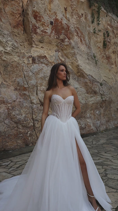 Princess A-line bridal gown with sleeveless sweetheart neckline, pearl-embellished sheer bodice, drop-down waist, slit skirt, and chapel train.