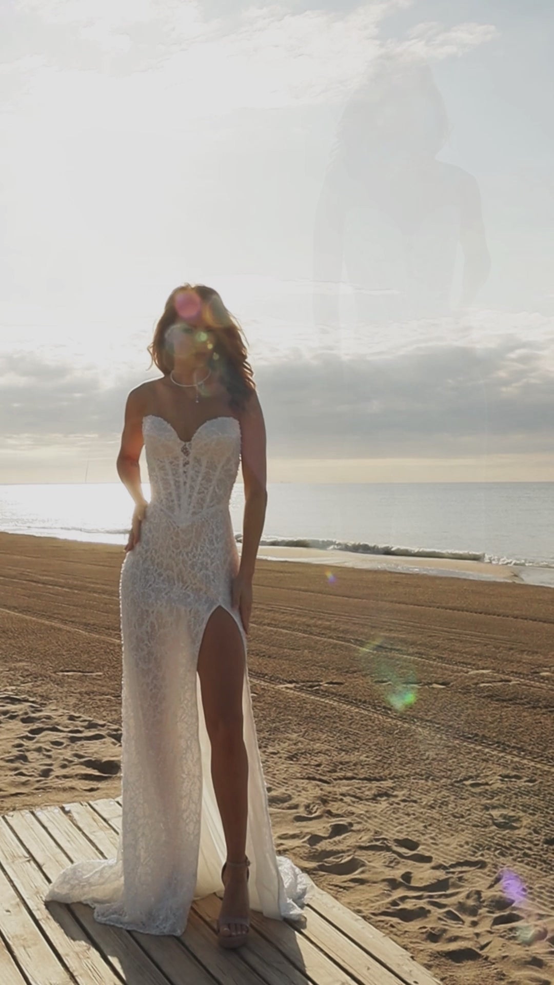 Bride in sleeveless lace bridal gown with sweetheart neckline, pearl and sequin embellishments, drop-down waist, slit skirt, zip closure, and sweep train.