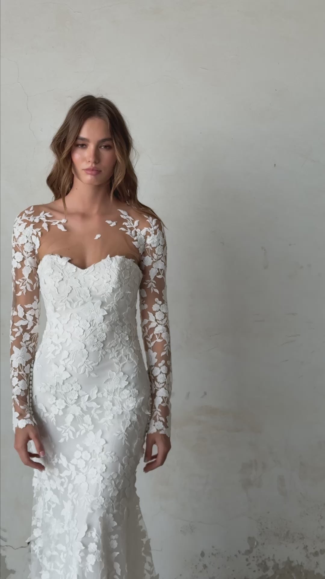 Bride in long-sleeve lace fit-and-flare wedding dress with floral appliqués, illusion back, and chapel train; styled with optional satin off-shoulder wrap.