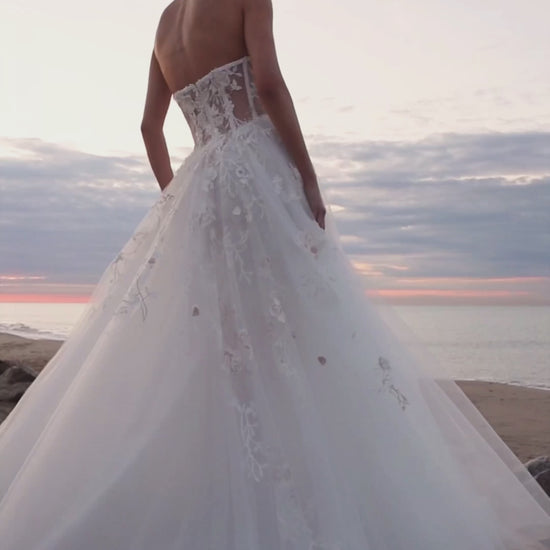 Bride in strapless floral lace and tulle A-line wedding gown with straight neckline, drop-down waist, and chapel train.