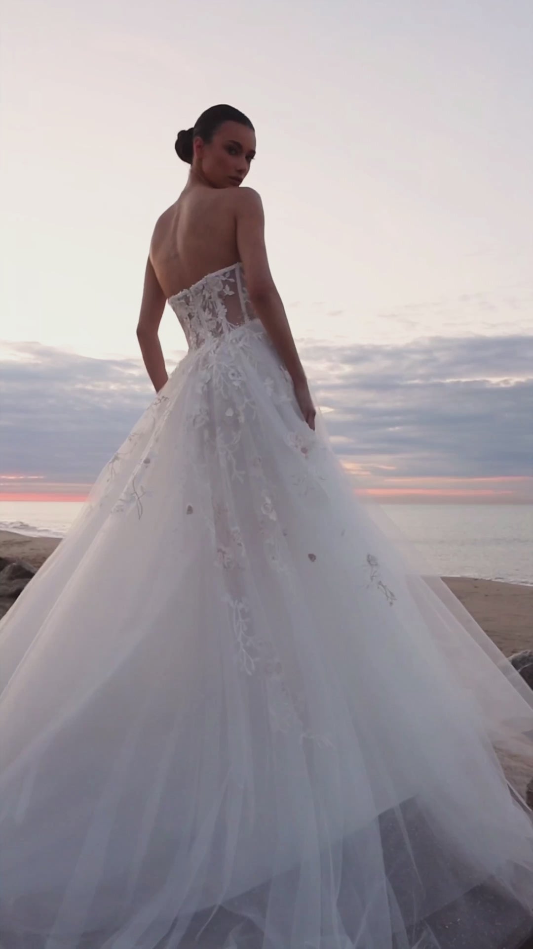 Bride in strapless floral lace and tulle A-line wedding gown with straight neckline, drop-down waist, and chapel train.