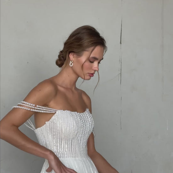 Pearl-embroidered tulle wedding dress with beaded corset bodice, detachable sheer sleeves, thigh-high slit, and flowing layered skirt