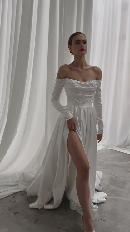Off-shoulder satin wedding dress with long sleeves and slit.
