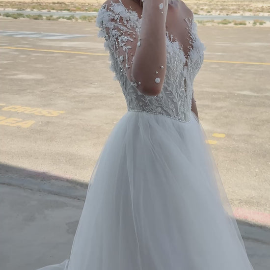 Bride wearing illusion tulle ball gown with 3D floral appliqués, pearl embroidery, and illusion back with buttons, photographed beside an airplane hangar.