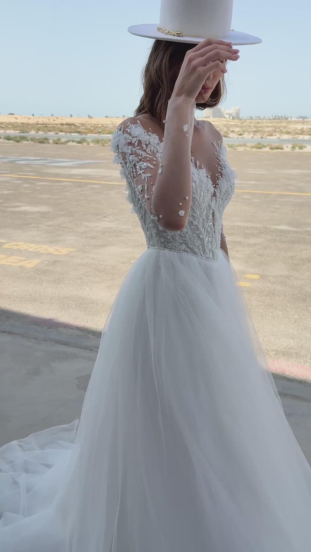 Bride wearing illusion tulle ball gown with 3D floral appliqués, pearl embroidery, and illusion back with buttons, photographed beside an airplane hangar.