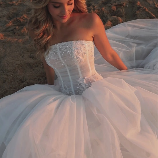 Bride in strapless soft tulle wedding gown with pearl and lace embellished prolonged bodice, zip closure, and chapel train.