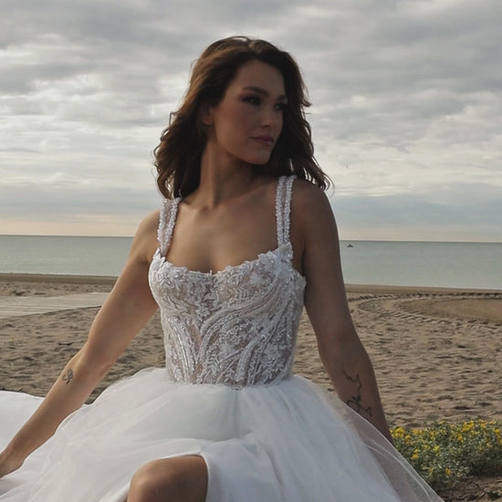 Sleeveless A-line bridal gown with boat neckline, lace bodice, wide straps, square back, glitter tulle slit skirt, and chapel train.