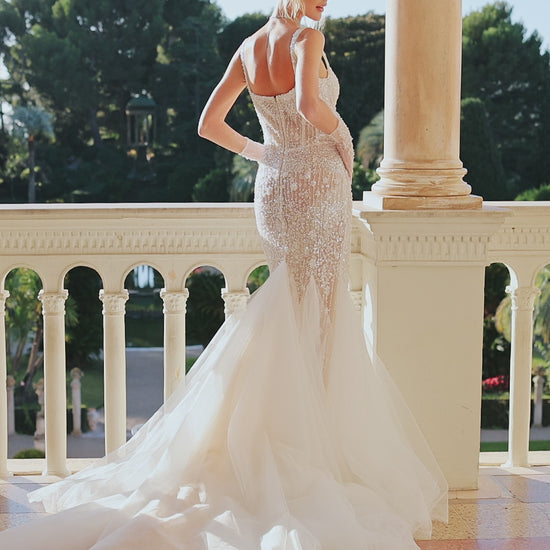 Sleeveless fitted wedding dress with square neckline, open back, lace appliques, bead and pearl embroidery, glitter tulle, and sweep court train.