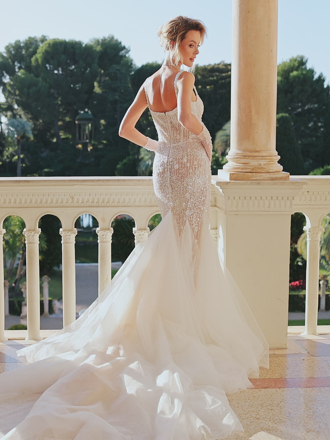 Sleeveless fitted wedding dress with square neckline, open back, lace appliques, bead and pearl embroidery, glitter tulle, and sweep court train.