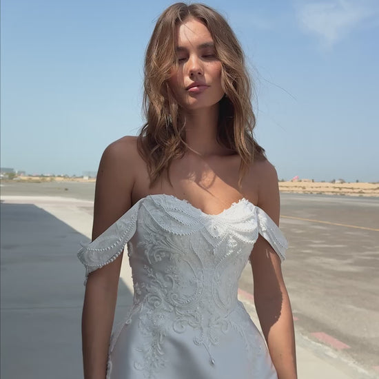Bride wearing off-the-shoulder Mikado A-line wedding gown with beaded lace bodice and flowing skirt, photographed at an airfield hangar.