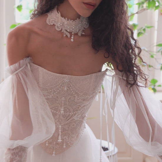 Bride wearing beaded corset A-line wedding dress with detachable tulle sleeves and flowing layered skirt.
