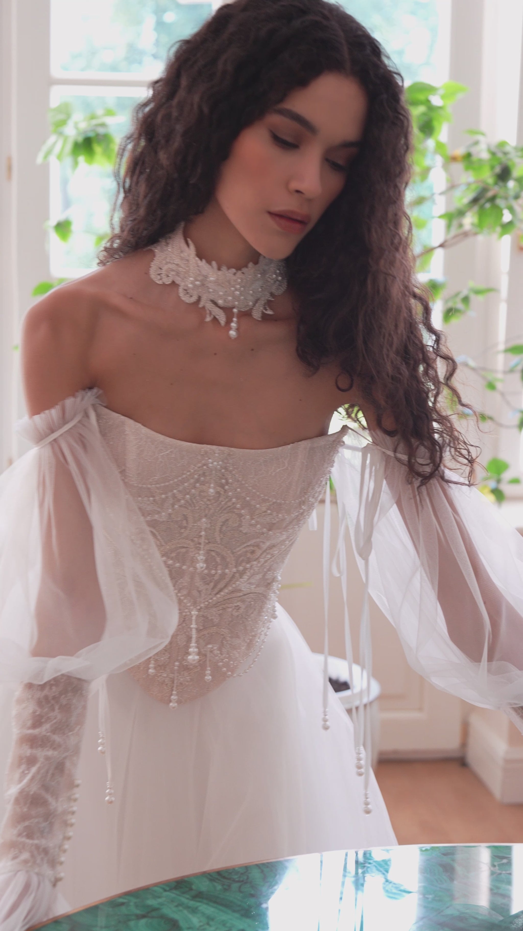 Bride wearing beaded corset A-line wedding dress with detachable tulle sleeves and flowing layered skirt.