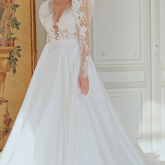  A-line wedding dress with puffy shoulder sleeves, V-shaped bodice, pleated skirt with pockets, embroidered belt, lace appliques, sequin details, and chapel train. Made of lace and taffeta mikado.