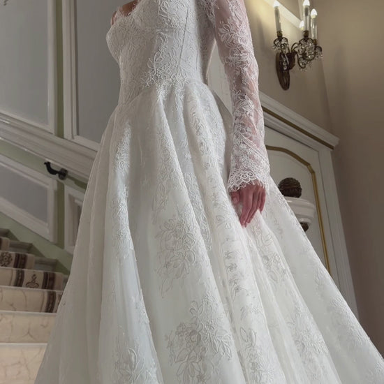 A-line floral lace wedding dress with an off-the-shoulder sweetheart corset, sheer long sleeves and a full skirt.