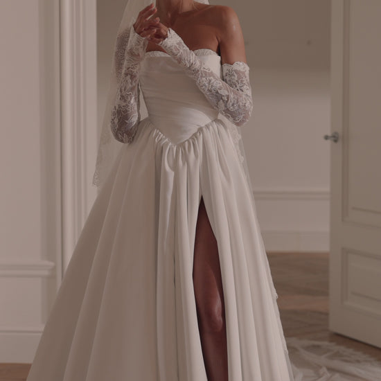 Bride wearing an off-shoulder A-line Mikado wedding dress with corset back, thigh-high slit, and chapel train.