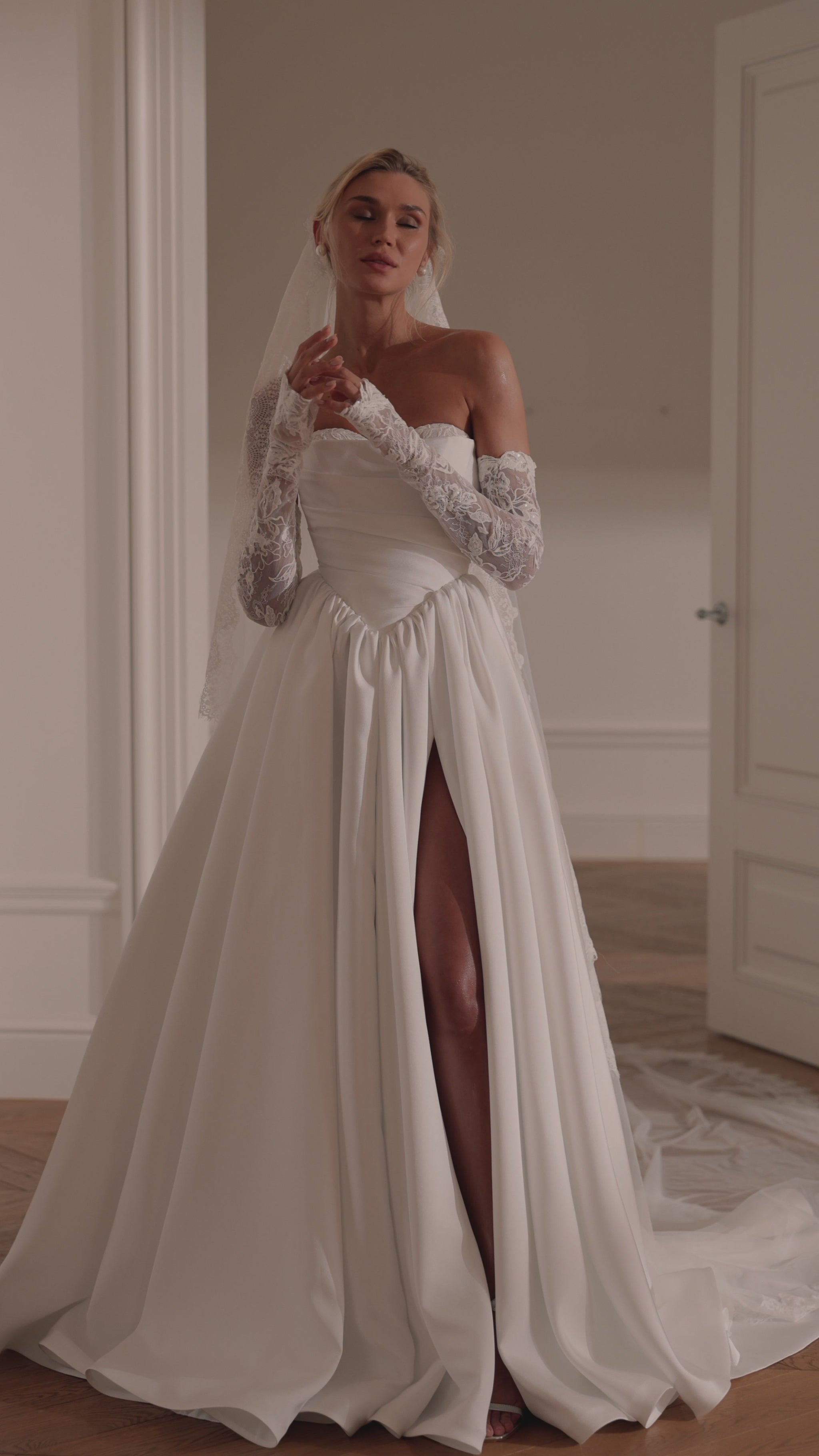 Bride wearing an off-shoulder A-line Mikado wedding dress with corset back, thigh-high slit, and chapel train.