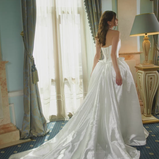 Bride wearing strapless taffeta corset wedding dress with pointed neckline, peplum waist detail, and full voluminous skirt.