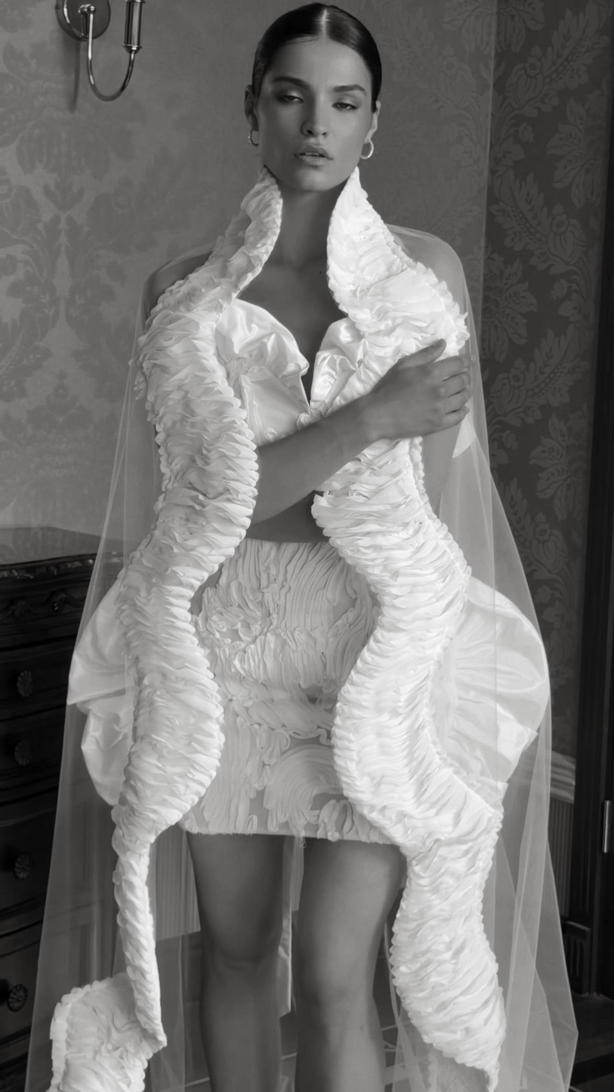 Mini wedding dress with a sweetheart corset bodice, sculptural ruffles and an optional sheer cape-veil.