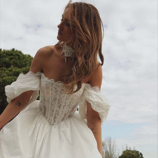Bride in princess A-line wedding gown with puffy off-shoulder sleeves, lace bodice, lace-up waist, plain taffeta skirt, and cathedral train.