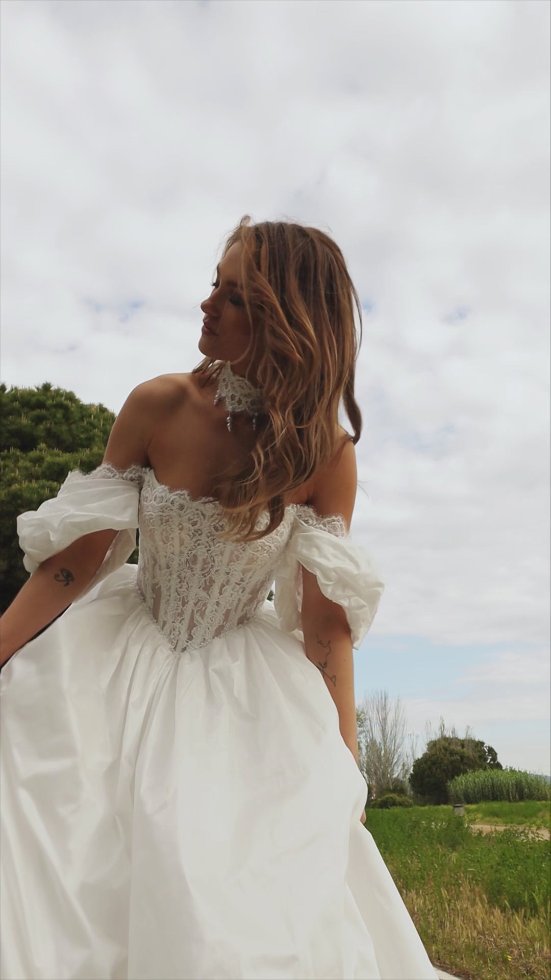 Bride in princess A-line wedding gown with puffy off-shoulder sleeves, lace bodice, lace-up waist, plain taffeta skirt, and cathedral train.