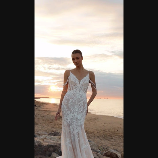 Bride in mermaid fit-and-flare lace wedding dress with pearl spaghetti straps, off-the-shoulder pearl strands, V-neckline, and sweep train.