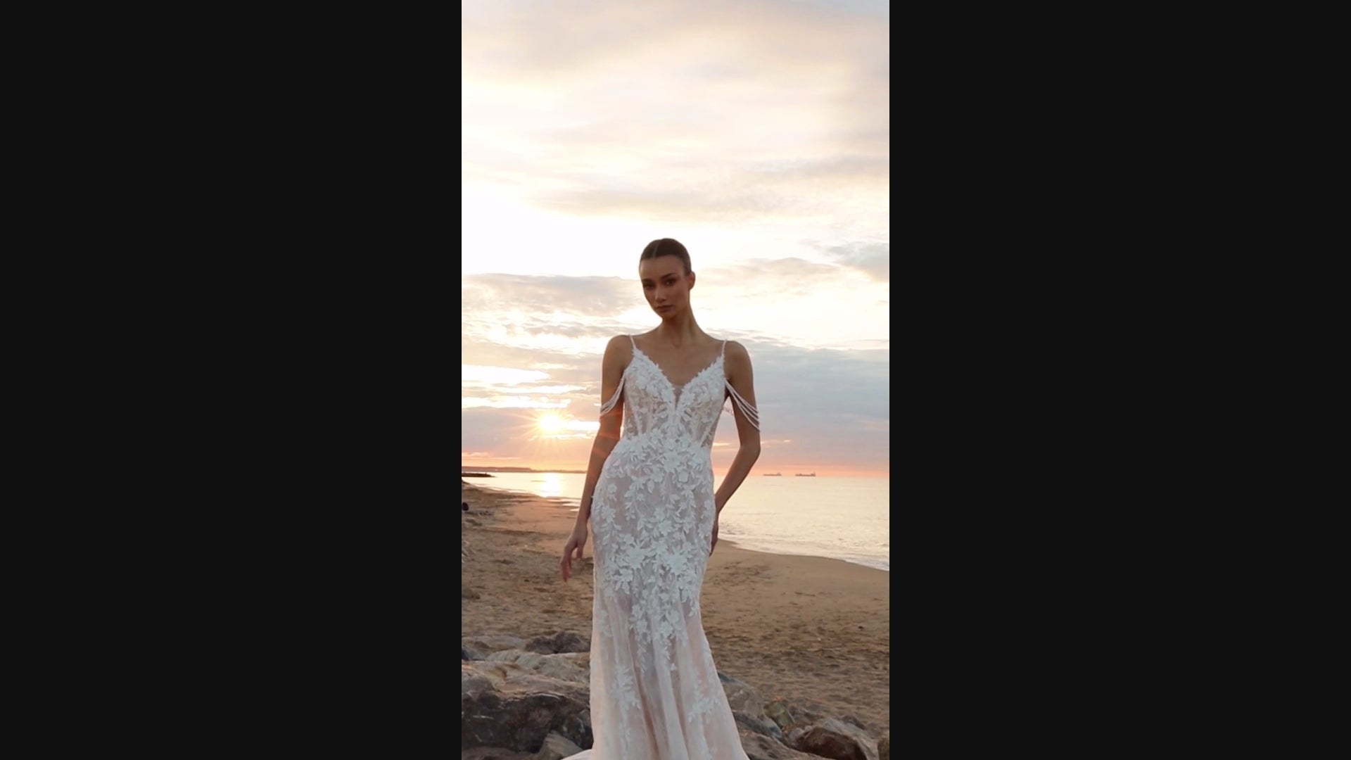 Bride in mermaid fit-and-flare lace wedding dress with pearl spaghetti straps, off-the-shoulder pearl strands, V-neckline, and sweep train.