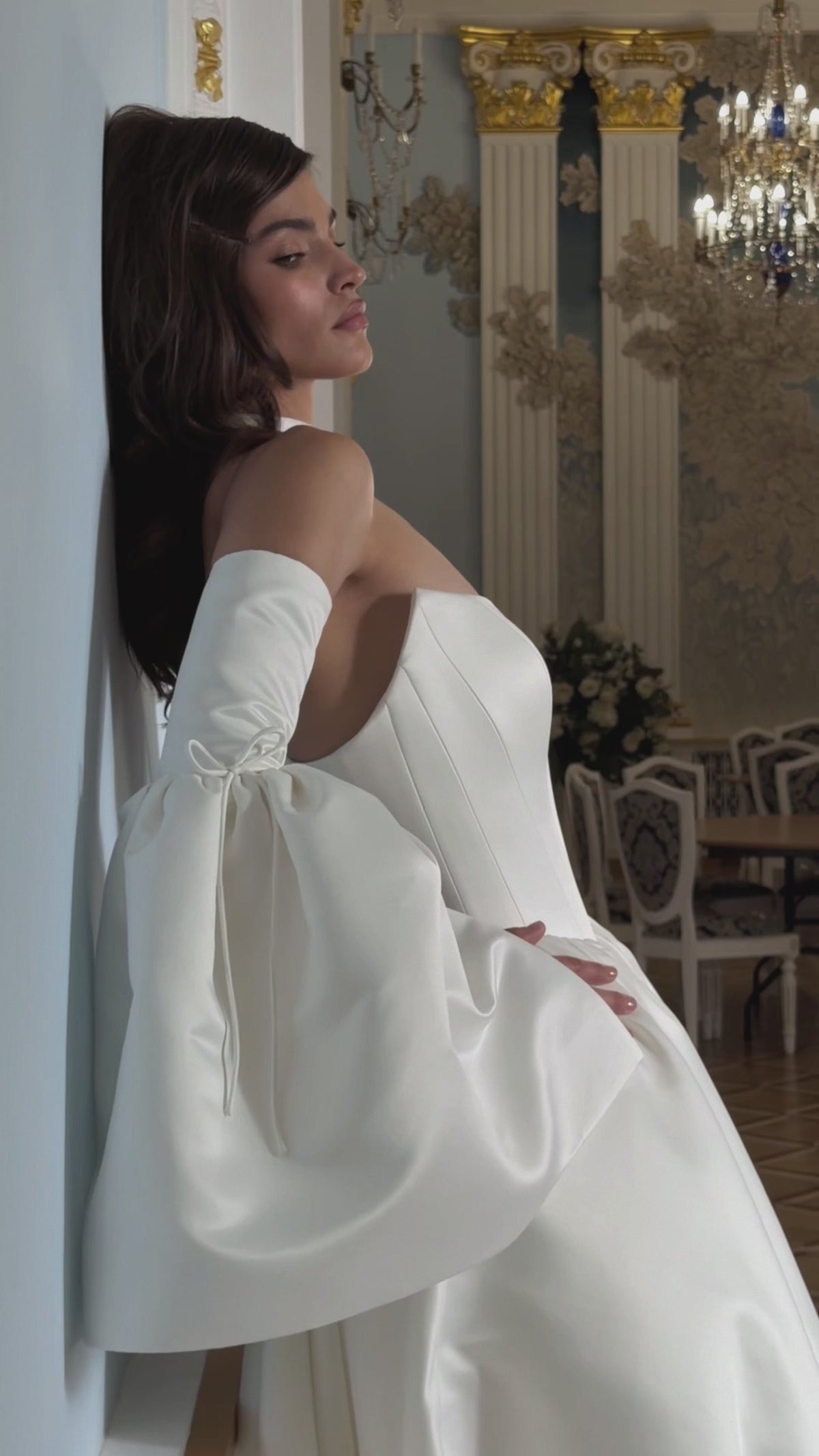 Video of an ivory basque waist wedding dress with a structured strapless bodice, detachable bell sleeves, bow choker and flowing skirt.