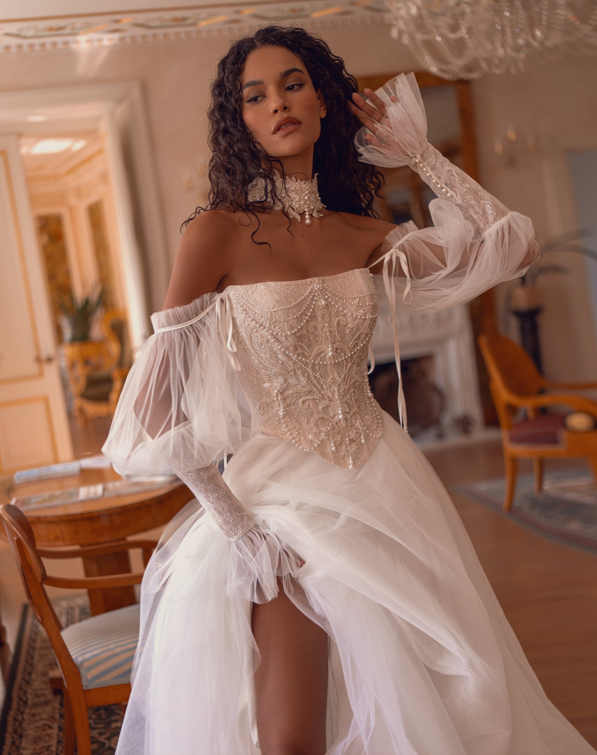 Bride wearing beaded corset A-line wedding dress with detachable tulle sleeves and flowing layered skirt.