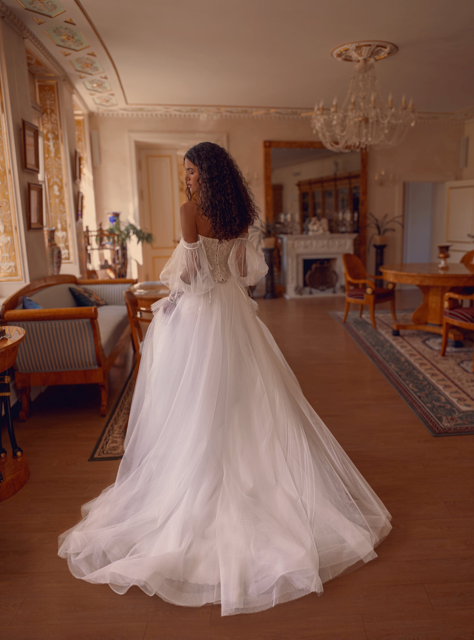 Bride wearing beaded corset A-line wedding dress with detachable tulle sleeves and flowing layered skirt.